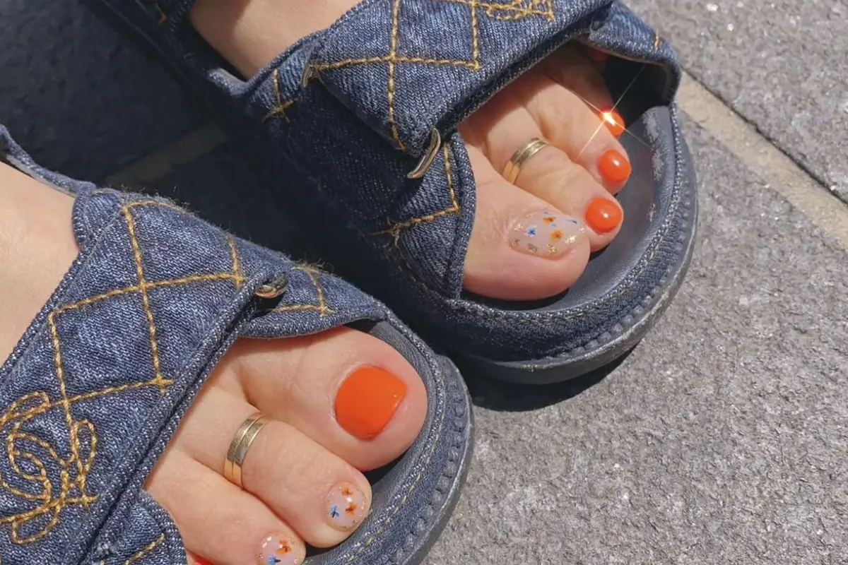 穿著牛仔布料的涼鞋與鮮艷的橙色和閃亮的銀色腳部美甲相互輝映。