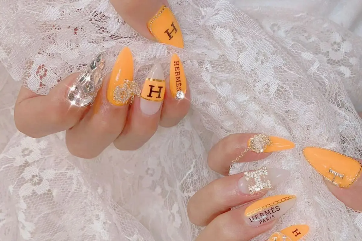 手部美甲設計以橙色為主打，搭配赫爾墨斯品牌圖案，展現時尚奢華。
