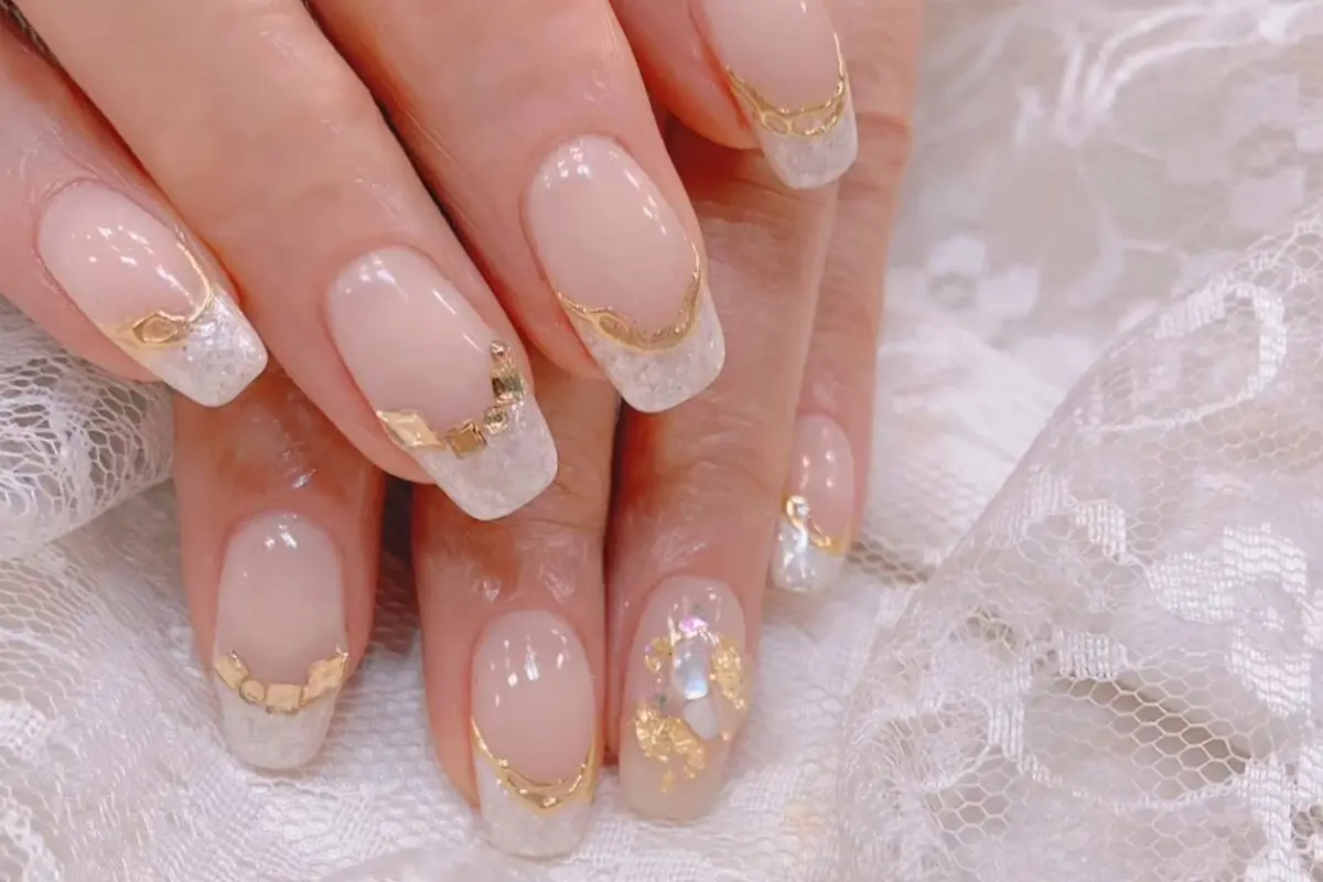 手部美甲展示優雅的白色和金色結合，搭配細緻的裝飾，創造高級感。
