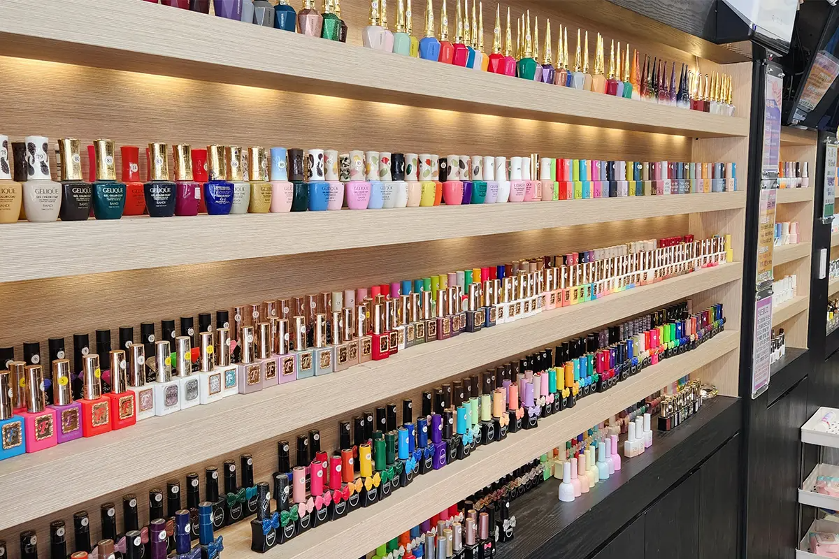 手部美甲展示多樣顏色的大量指甲油瓶排列在架子上，色彩繽紛，選擇多樣。