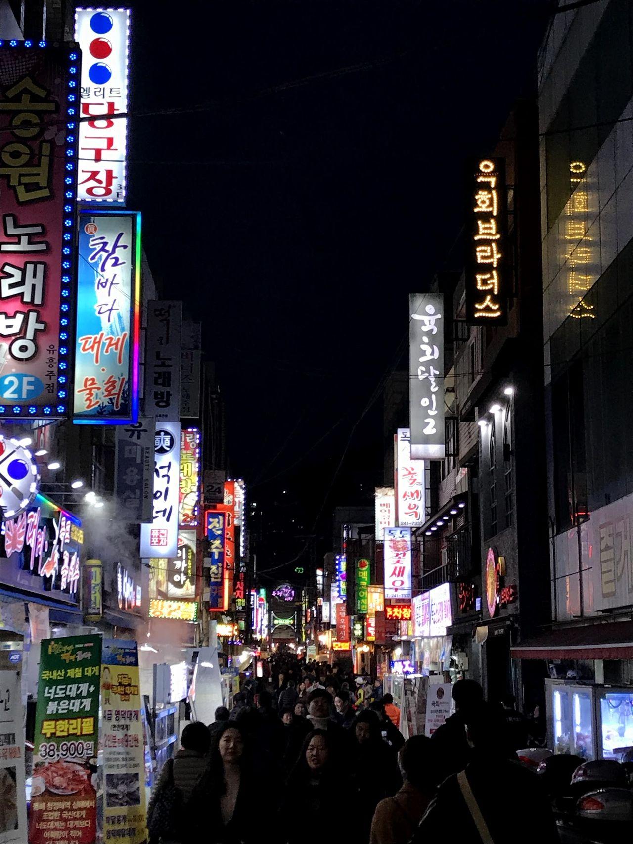 釜山繁华街区的夜晚景象，街道灯火通明，人流如潮。