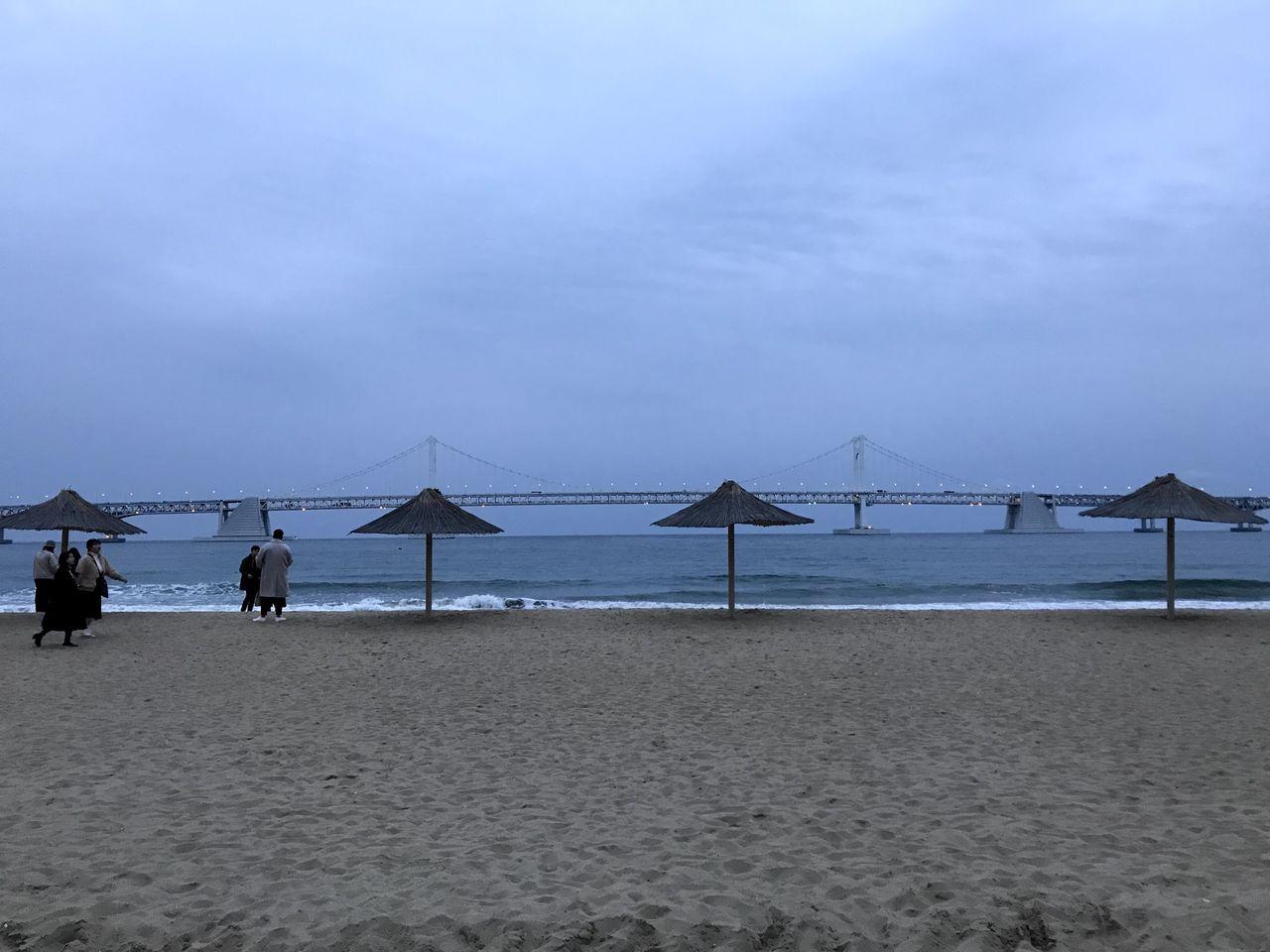 广安大桥后面的沙滩景观，沙滩伞树立，海浪轻拍岸边。