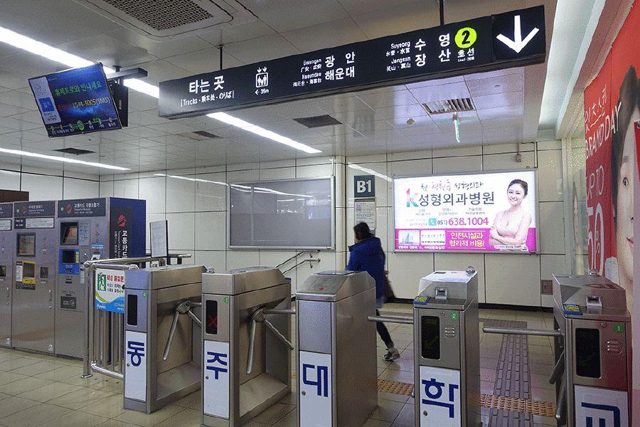 釜山地铁站内部，乘客通过闸机，电子显示屏和地铁线路标识清晰可见。