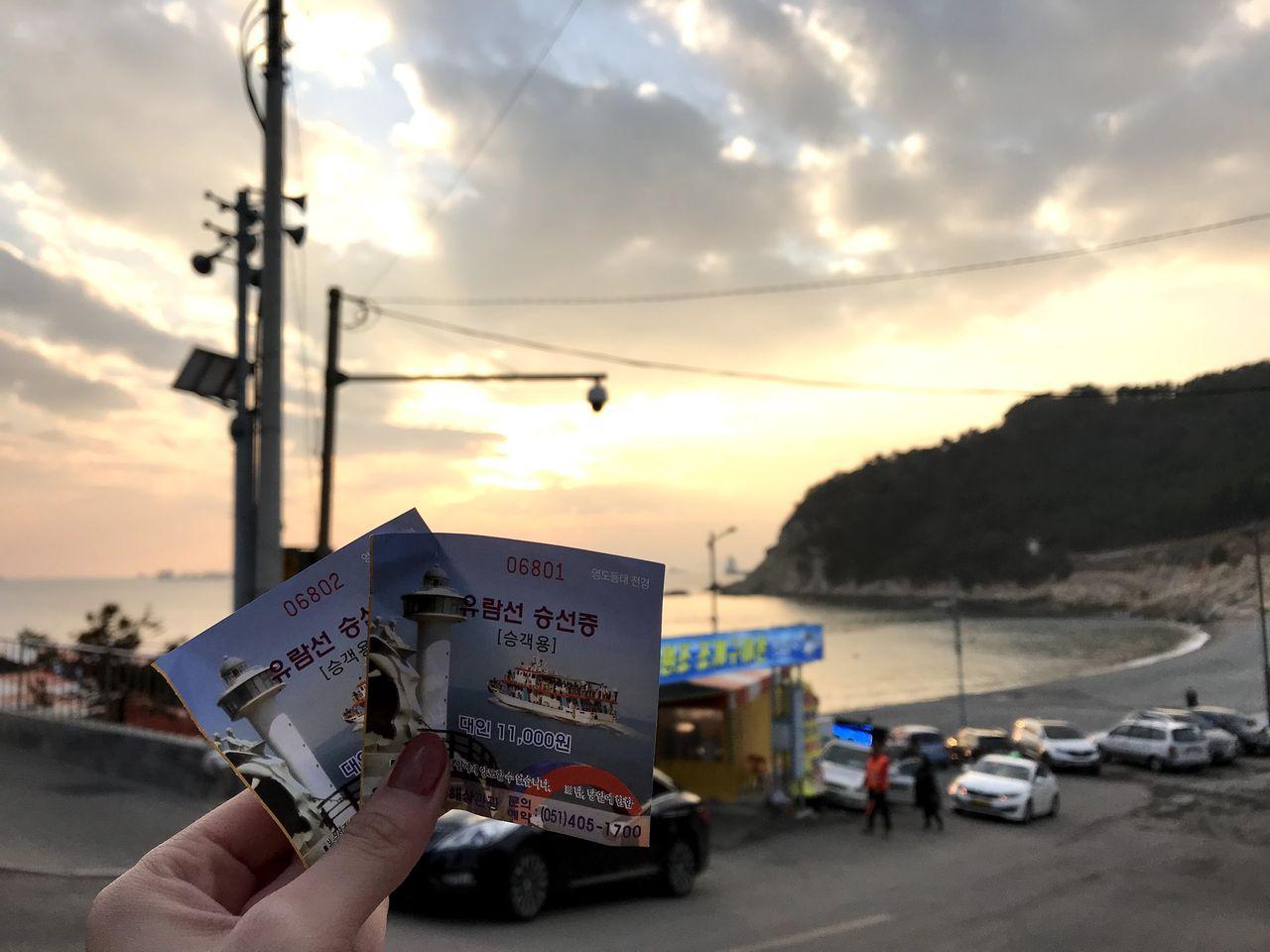 夕阳中的太宗台，游客手拿船票在海岸边拍照留念。