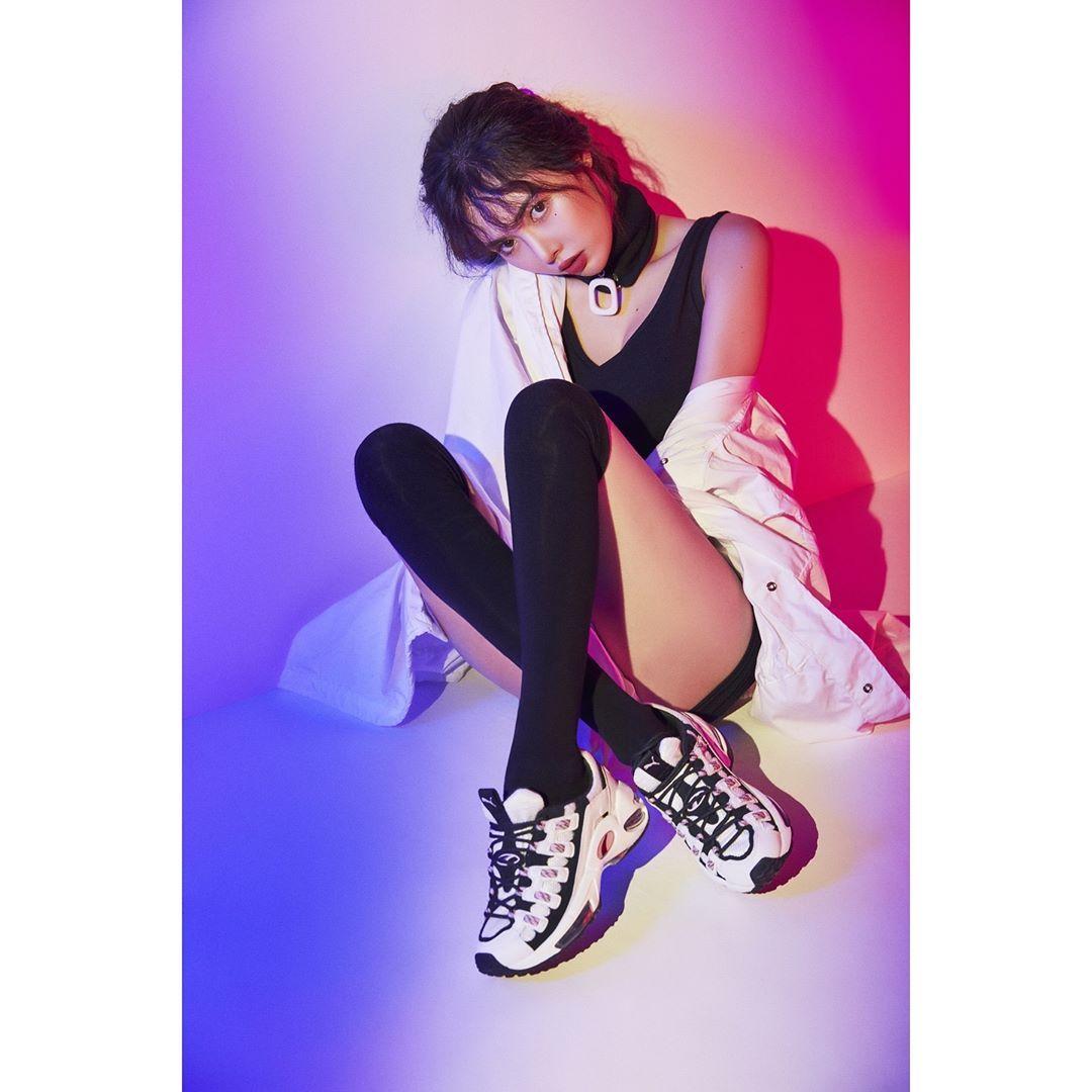 泫雅身著黑色運動上衣，搭配PUMA運動鞋，呈現出強烈的時尚運動風格，背景為粉色調配。