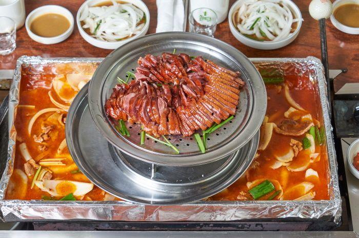 Half-and-half dish featuring smoked duck and spicy duck soup served with side dishes.