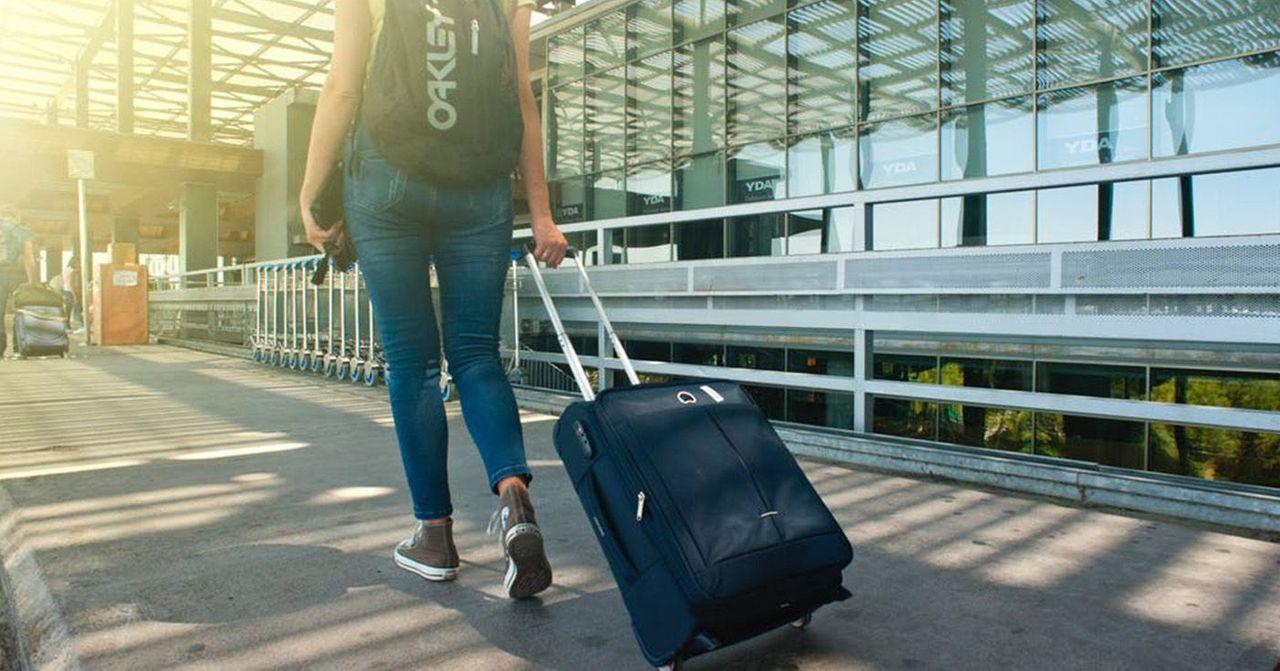 机场背景下一名旅行者拖着手提箱，为了遵守新规定准备申报物品。