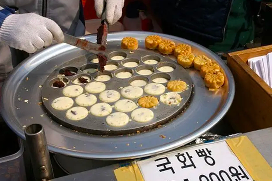 Cooking process for Korean Kukhwabang, small flower-shaped pastries, being filled with red bean paste on a grill.