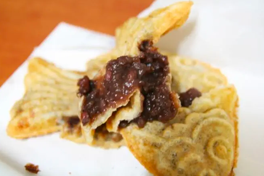 Korean fish-shaped snack, Bungeoppang, cracked open to reveal sweet red bean filling, showcasing the delicious texture inside.