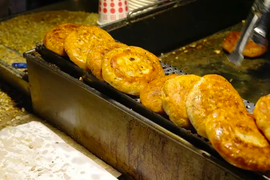 Several Hotteok pancakes cooking on a street food grill, showcasing the traditional Korean sweet treat's rich golden color.