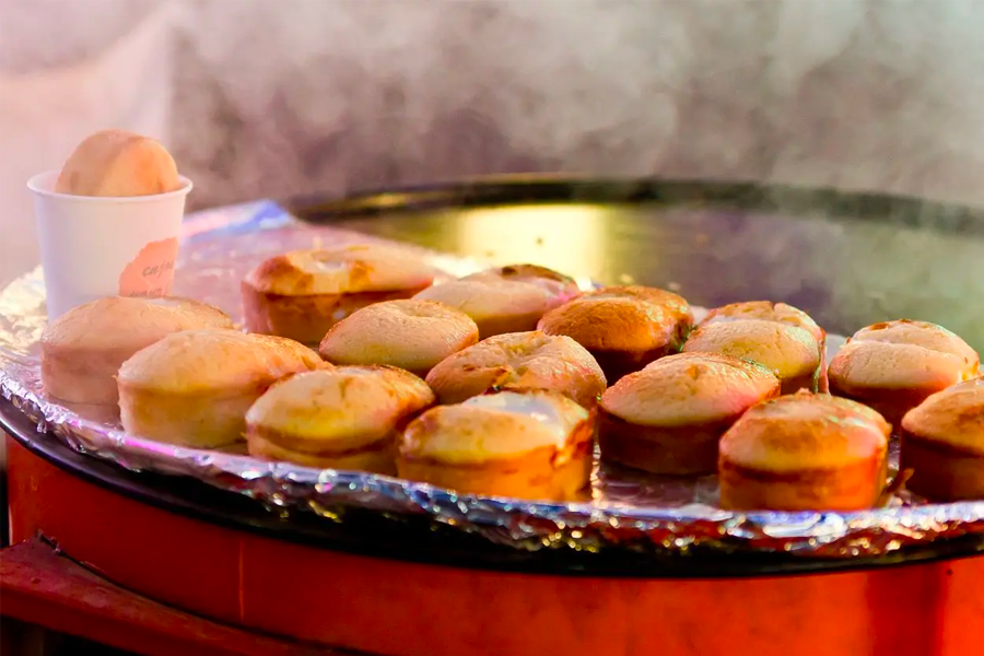 Korean Gyeranppang, steamy and fresh egg cakes with entire eggs inside, cooking on an open grill.