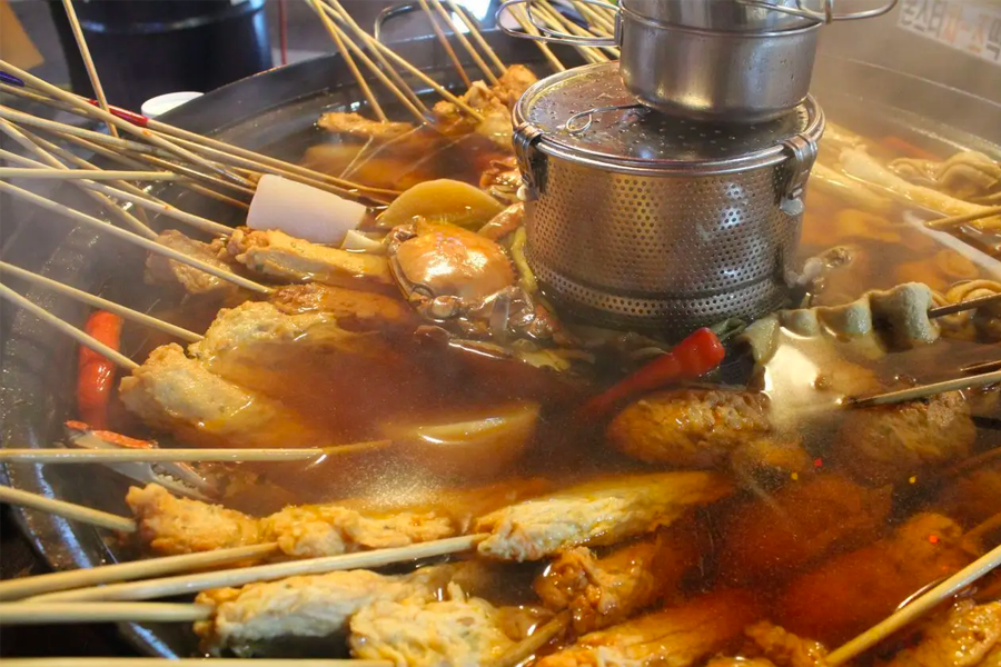 Close-up of Korean fish cake soup with various skewers submerged, a classic street food dish enjoyed widely.