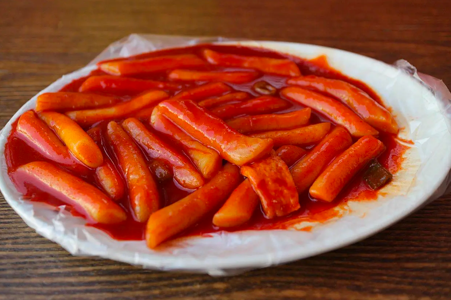 Plate of Korean Tteokbokki, chewy rice cakes bathed in spicy sauce, a beloved street food dish for its fiery taste.