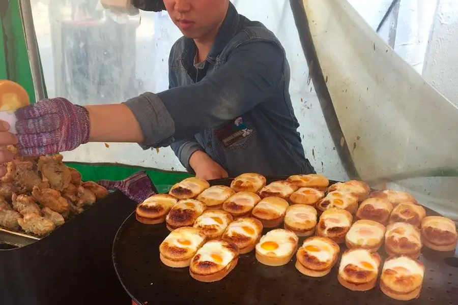 Street vendor arranging Korean Gyeranppang, oval-shaped egg cakes, on a grill for passersby in bustling areas.