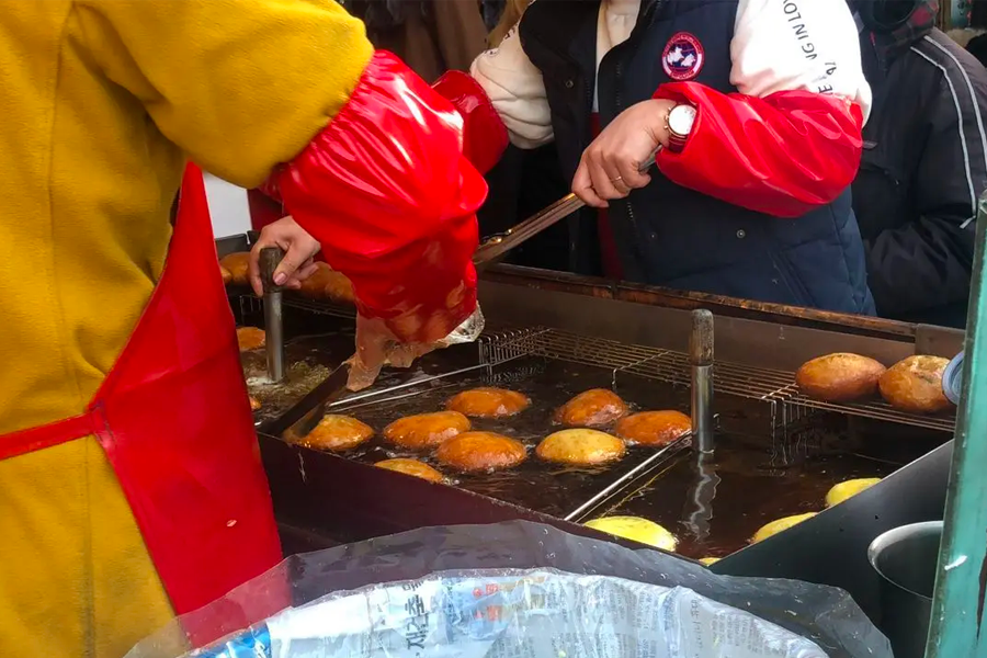 Vendor frying Korean street snack Hotteok, crispy pancakes filled with sweet sugar and cinnamon on a griddle.