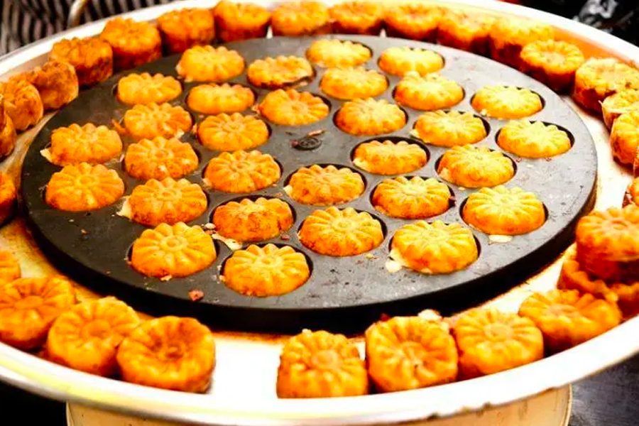 Korean street snack Kukhwabang, flower-shaped pastries baking on a grill, a sweet delight during festivities.