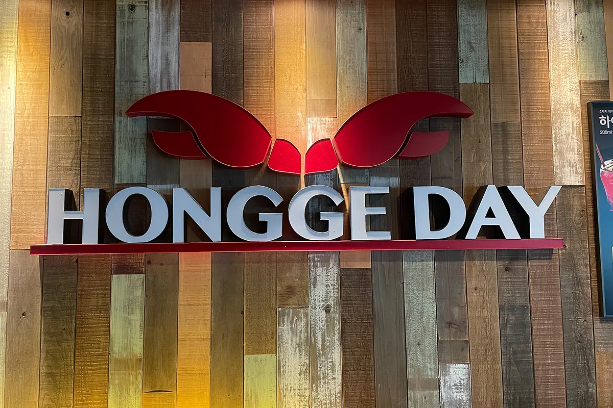 深紅色的標誌擺設於木質牆壁上，標誌上寫著「Hongge Day」字樣。