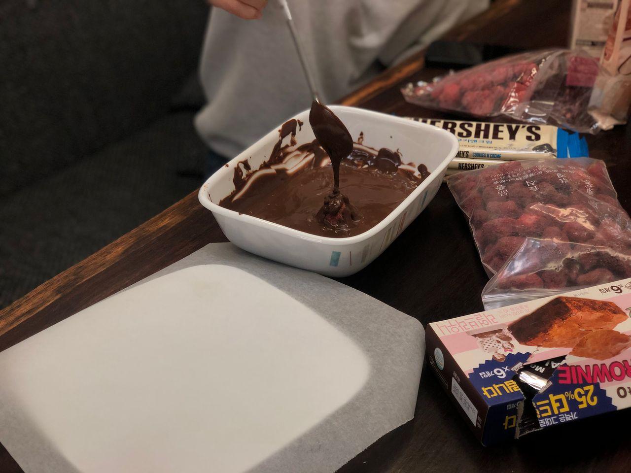 在準備融化的朱古力混合物中攪拌，在旁邊備有士多啤梨乾和其它巧克力材料，為製作巧克力士多啤梨甜點做好準備。