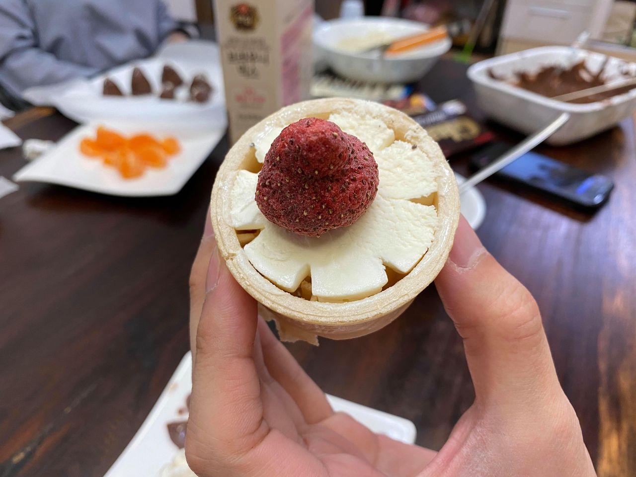 手持甜筒雪糕，頂部裝飾著韓國士多啤梨乾，顯示出甜品的精美製作。