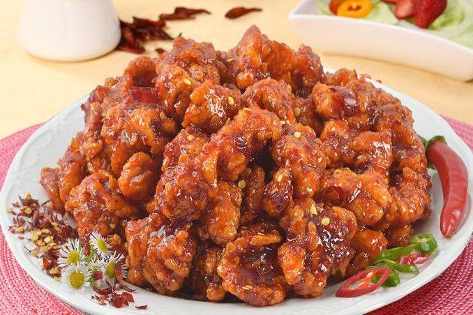 一盤鬧烈紅辣椒醬炸雞擺放在白色盤中,旁邊配有辣椒和草莓點綴。