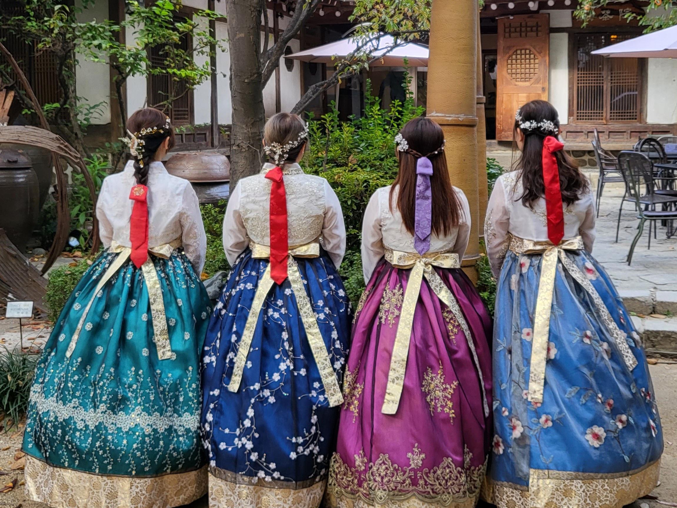 四位背對鏡頭的女性身穿色彩繽紛的韓服，展示韓國傳統服飾的精美設計。