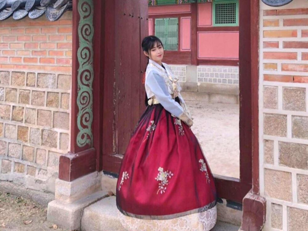 A woman in a beautiful, flowing hanbok posing against a serene backdrop of nature, highlighting the fusion of Korean tradition and natural beauty at Princess Hanbok.