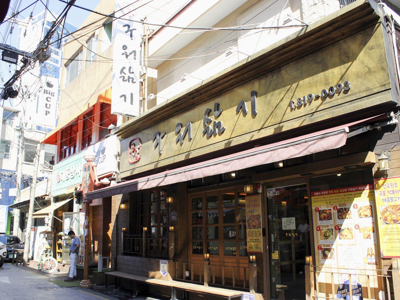 釜山“烤了又煮”餐廳外觀，白天，建築的金色招牌上面寫著店名，吸引著路人目光