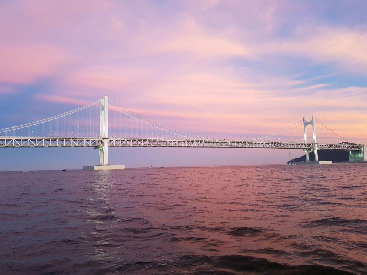 釜山廣安大橋在日落時分呈現美麗的粉色色調，海面平靜映出橋樑的倒影。