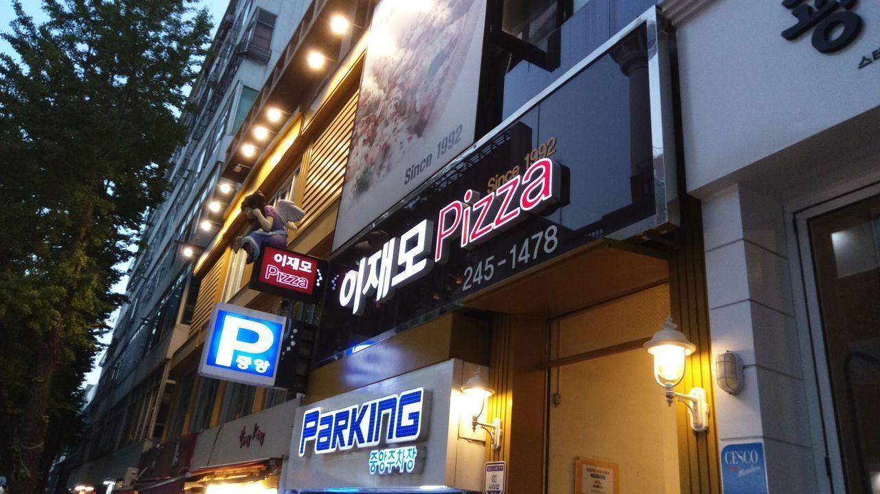 釜山的LEE JAE MO披薩店外觀，夜景中霓虹燈標識清晰可見。