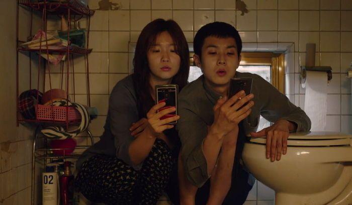 《寄生上流》电影场景，角色在卫生间使用手机。