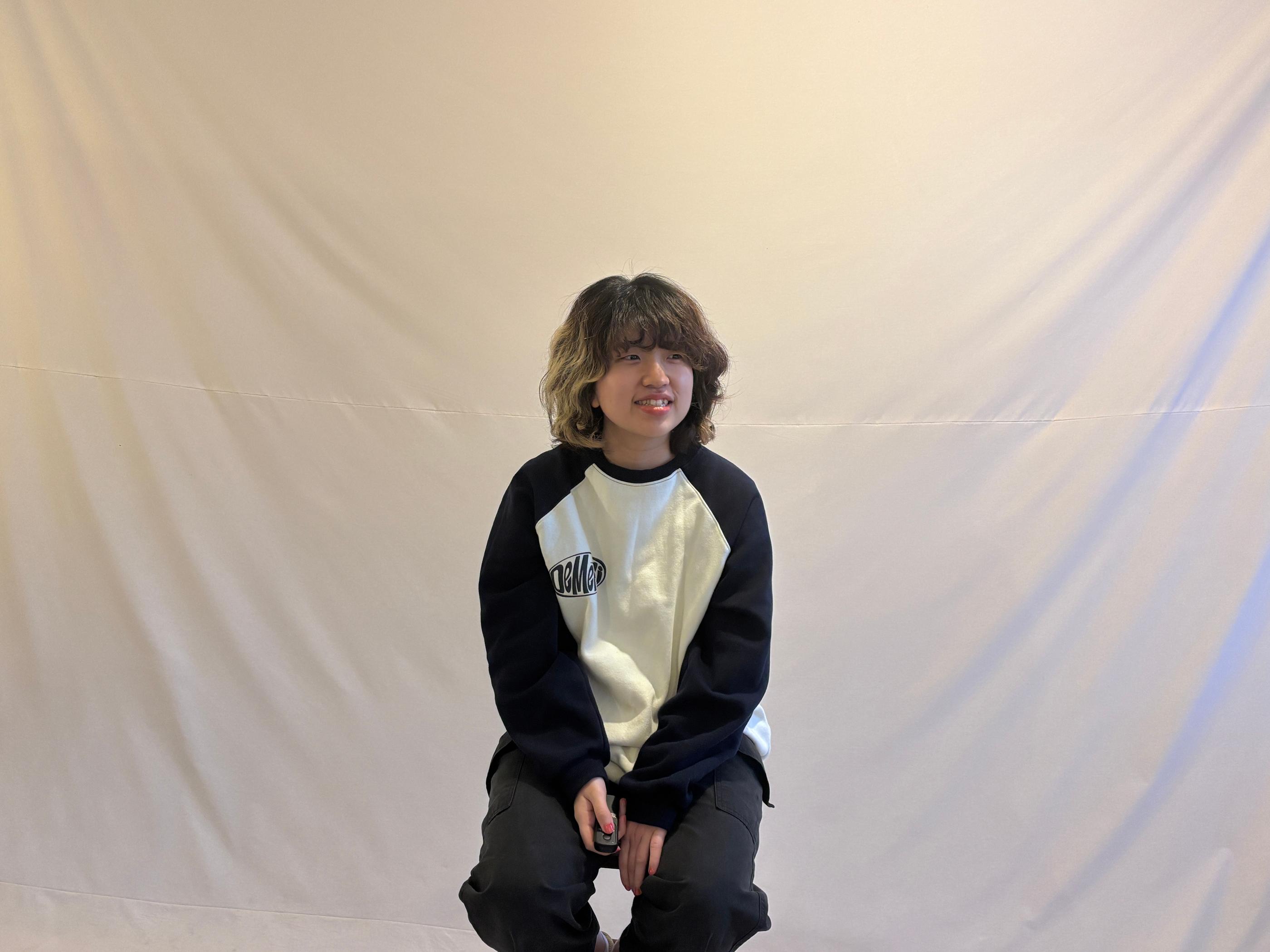 Cheese Smile Studio內的一位顧客坐在白色背景前，手持拍攝遙控器，準備進行自助拍攝。