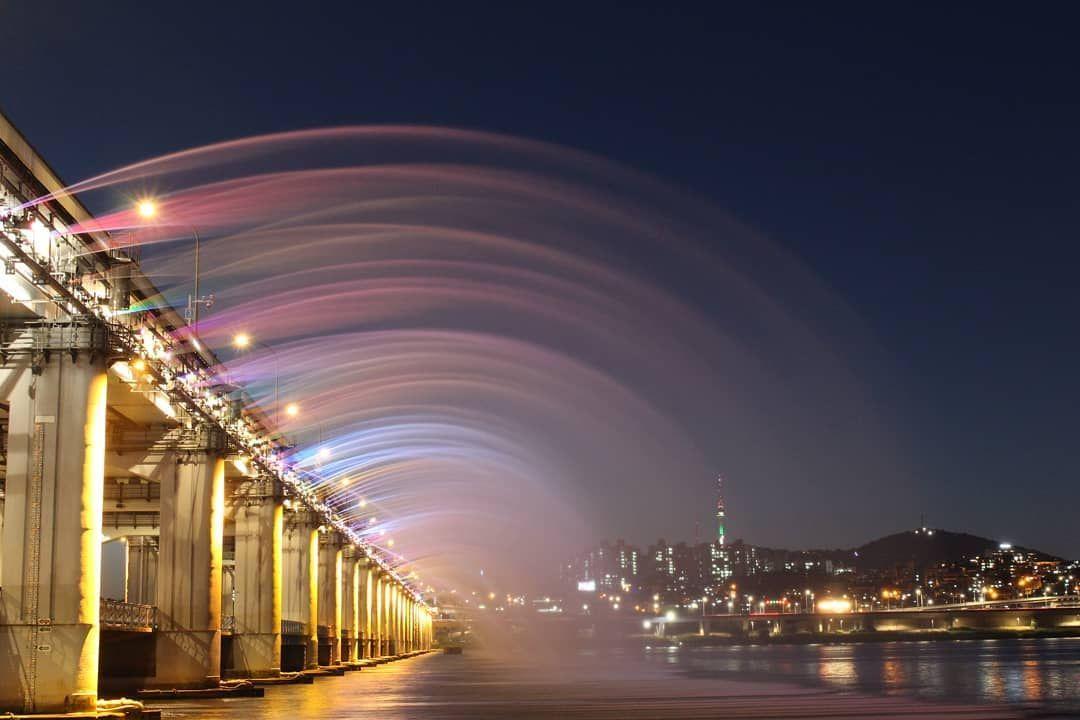 Colorful water jets of the Banpo Bridge Rainbow Fountain Show illuminated at night over the Han River in Seoul.