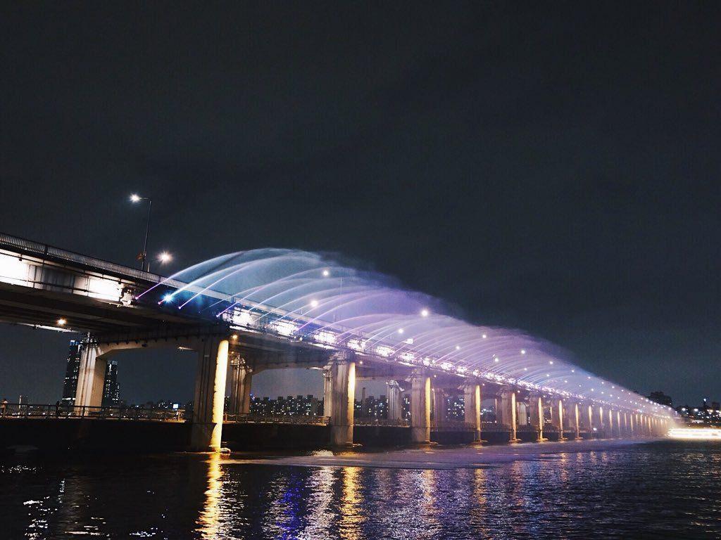 Night view of Banpo Bridge Rainbow Fountain in Seoul reflecting on the Han River, creating a picturesque scene.