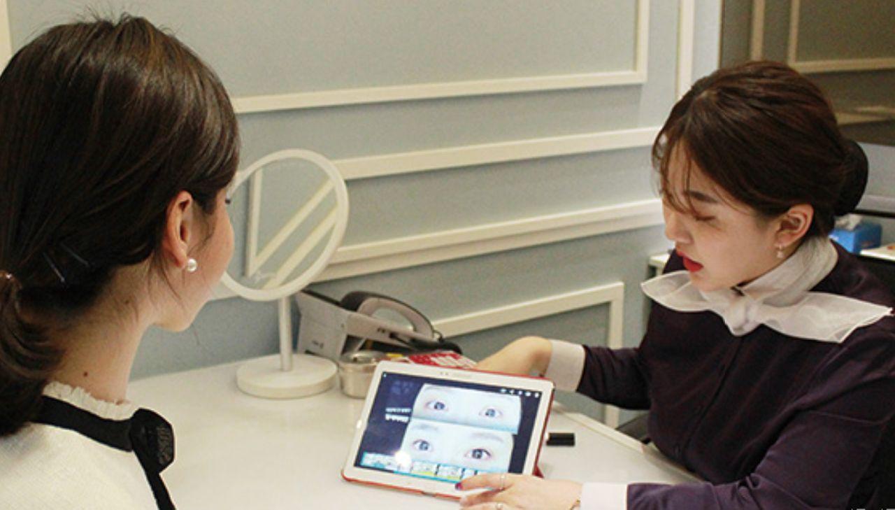 Customer discussing semi-permanent eyebrow options with a consultant using a digital presentation at Juliet Beauty, Busan.
