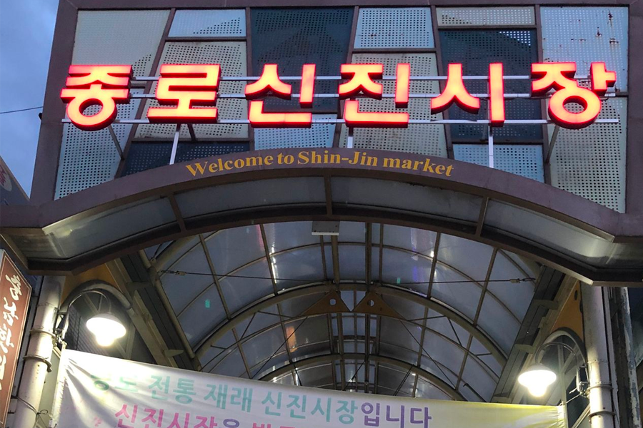 首爾鐘路新進市場入口，歡迎光臨的新進市場招牌和前方的帳篷上方韓文標示，晚上拍攝的市場門口特寫。