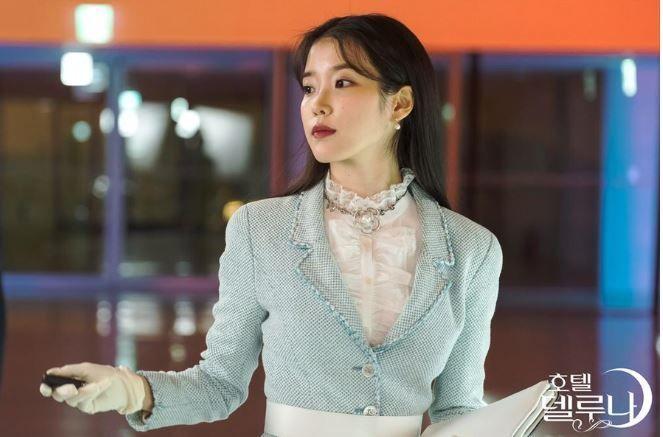 Personnage de 'Hotel Del Luna' aux cheveux longs et dressés dans une tenue glamour sous la lumière douce du salon.