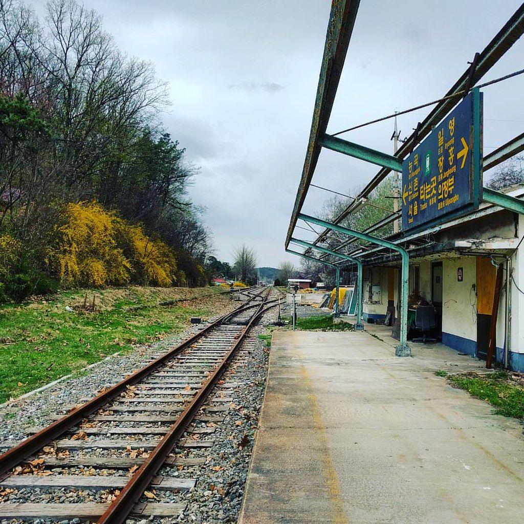 Vue du quai de la gare de Byukje avec des rails de train et de la végétation autour.