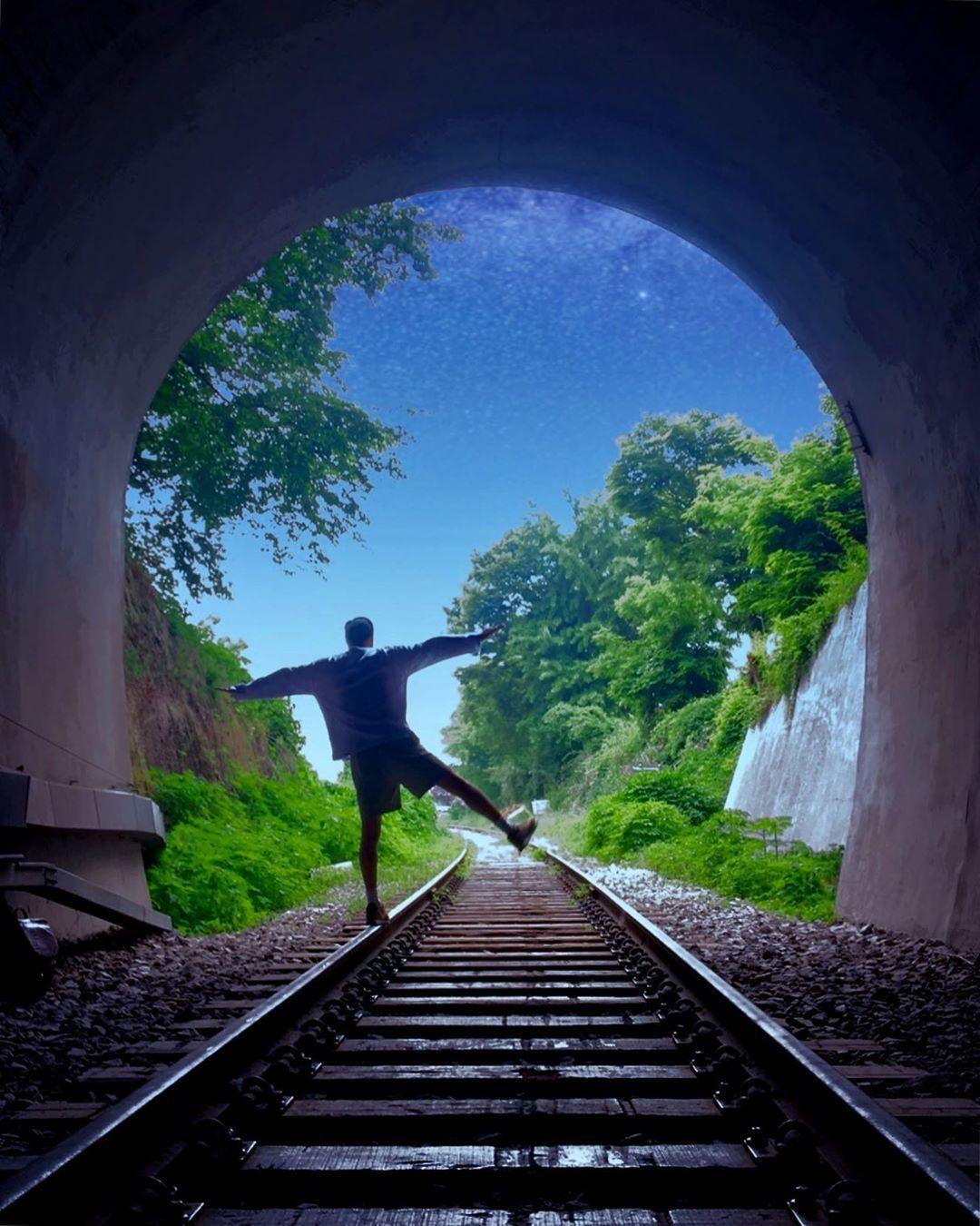 Homme dansant joyeusement sur les rails à l'intérieur du tunnel de la gare de Byukje, sous un ciel étoilé en arrière-plan.