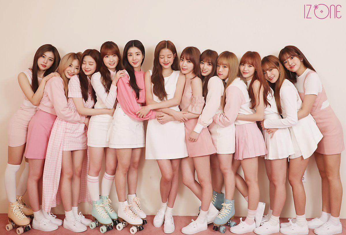 ภาพสมาชิกวง IZ*ONE ในชุดสีชมพูและสีขาว ขณะถ่ายภาพร่วมกันเป็นกลุ่มใหญ่สะท้อนความเป็นทีม 