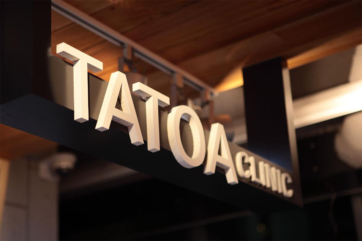 TATOAクリニックの看板。訪問者を迎える明るいLEDライトがある木の背景の看板。