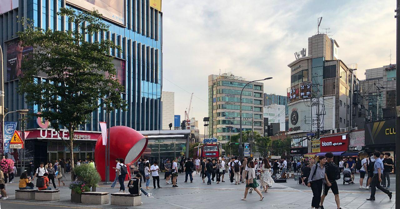 新村商圈的活力照片，行人走過寬闊的街道，背景是現代化的建築設計，充滿都市氣息。