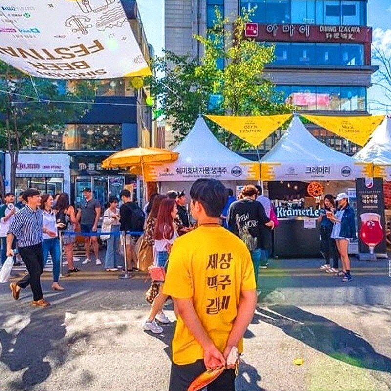 新村啤酒節上，工作人員穿著印有啤酒節標語的黃色T恤，背景是熱鬧的啤酒節攤位。