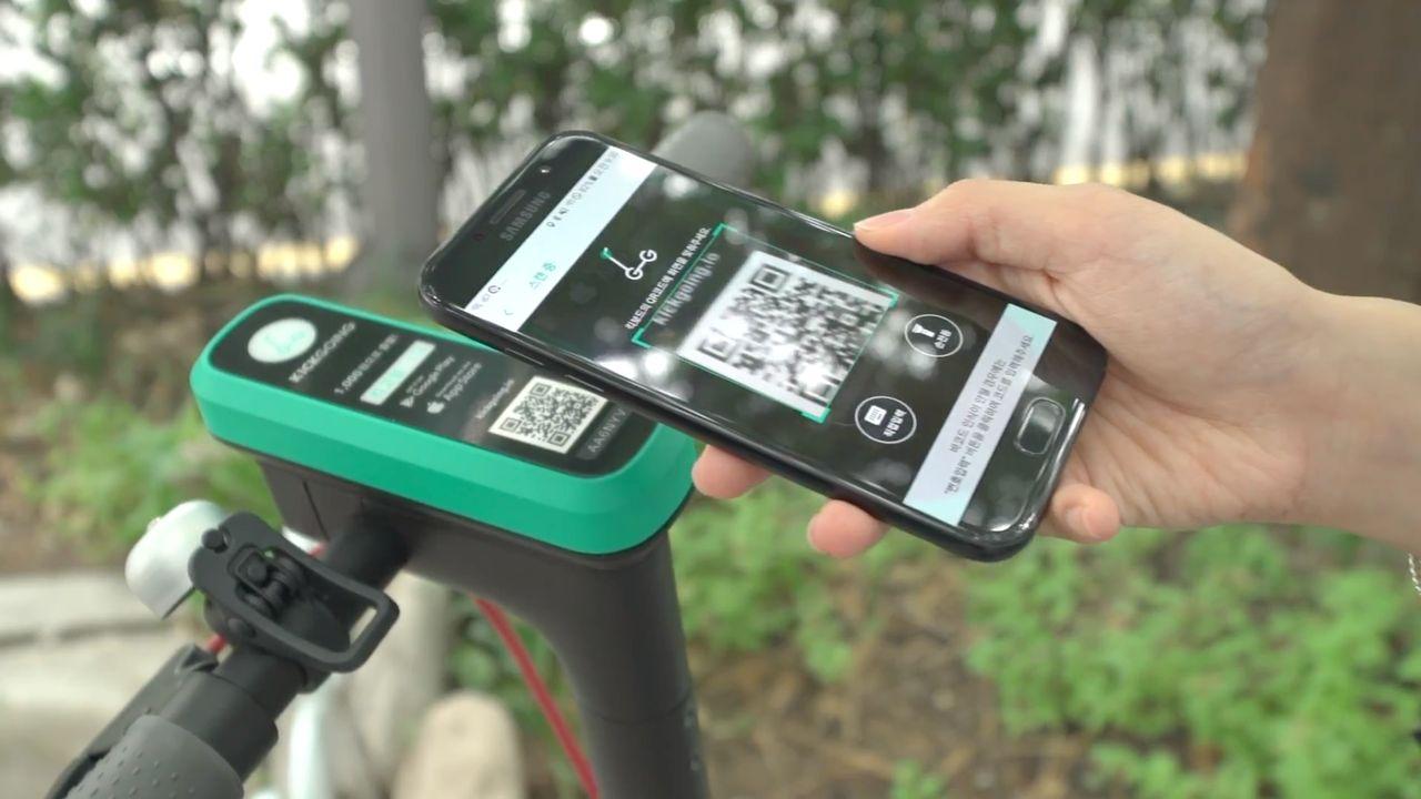用户正使用手機掃描共享滑板車上的 QR 碼，以便開始租用過程。