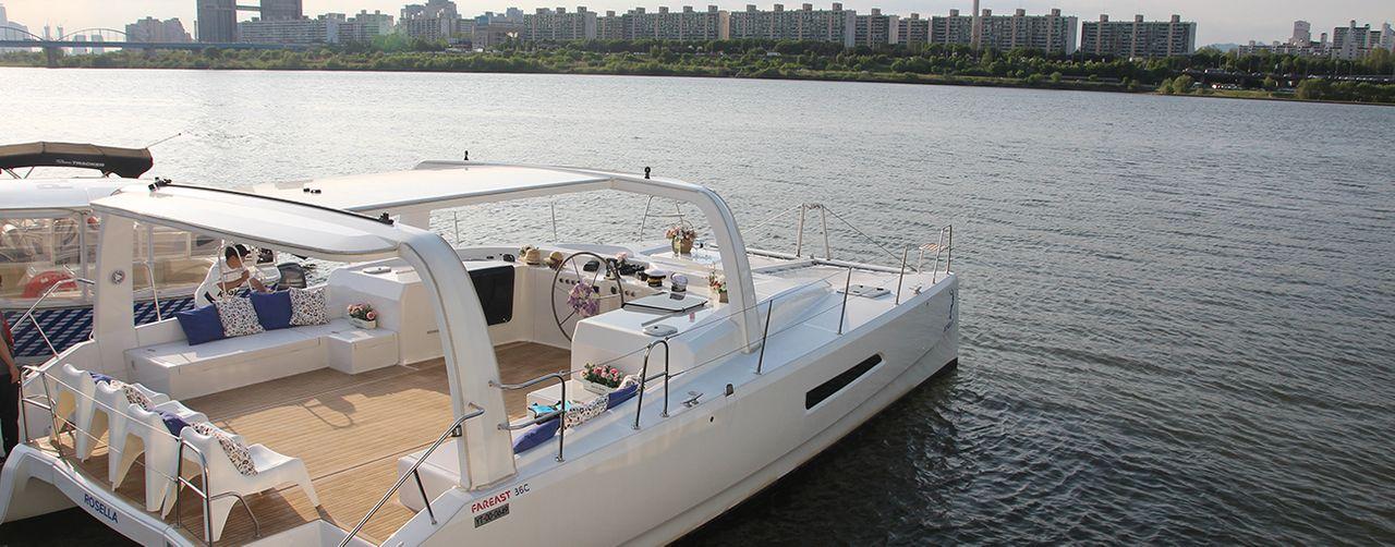 Immagine di uno yacht dal design moderno sulla superficie calma del fiume Han con lo skyline di Seoul sullo sfondo.