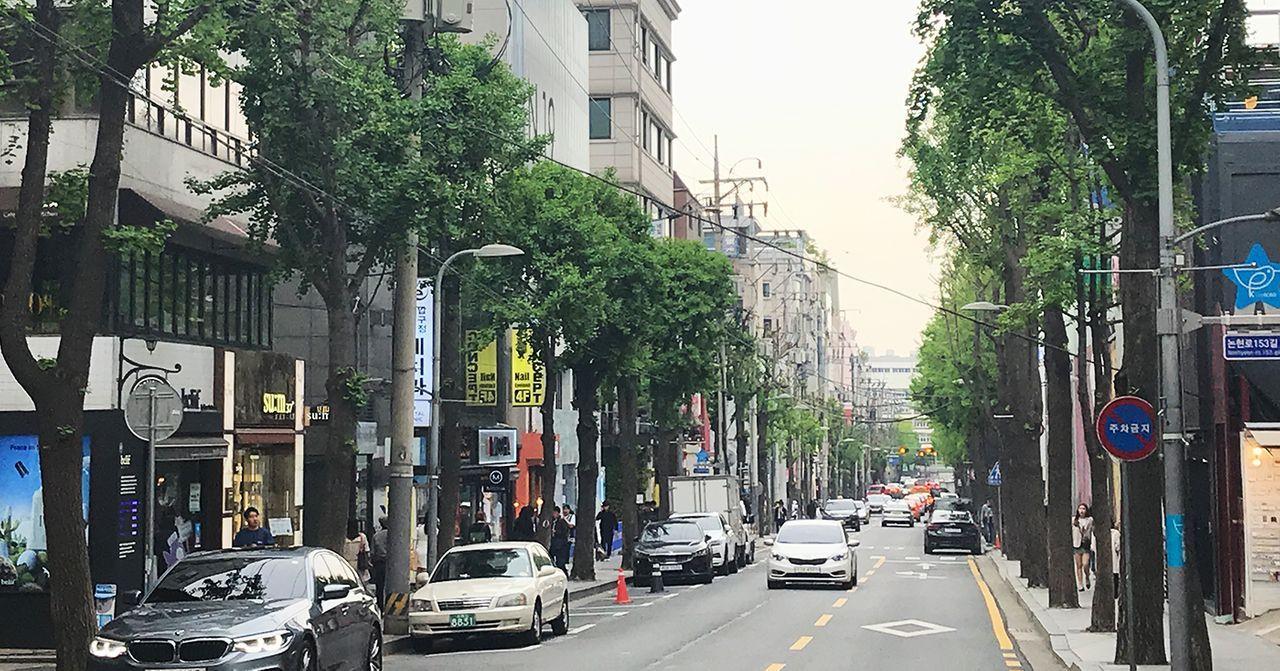 ถนนเกาหลีที่มีรถและคนเดินริมถนนท่ามกลางบรรยากาศที่มีแสงแดดอ่อนในฤดูร้อน