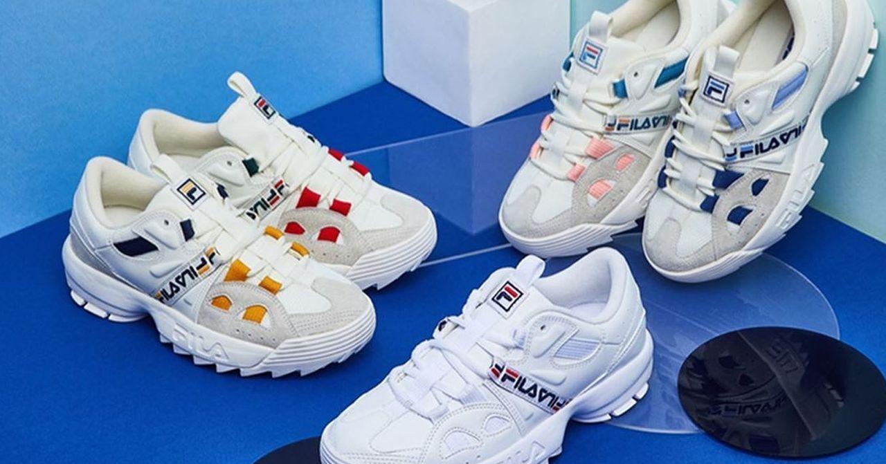 รองเท้าผ้าใบ Fila หลายคู่ในสีสันที่หลากหลายจัดวางบนพื้นผิวสีฟ้า