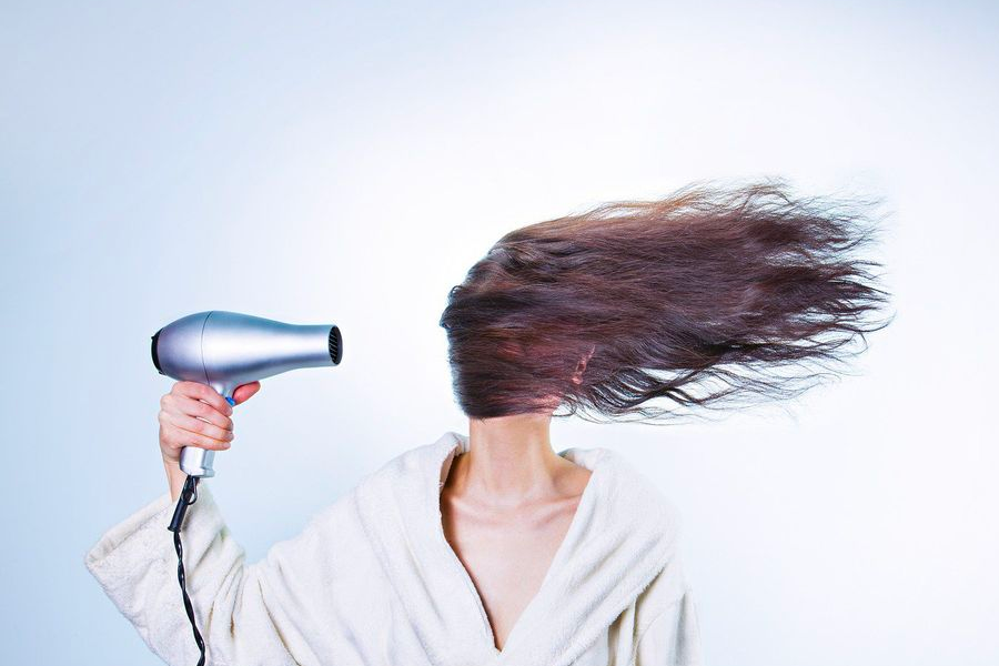 使用吹風機吹乾頭髮，旨在提醒電器需要轉接頭與變壓器才能使用。