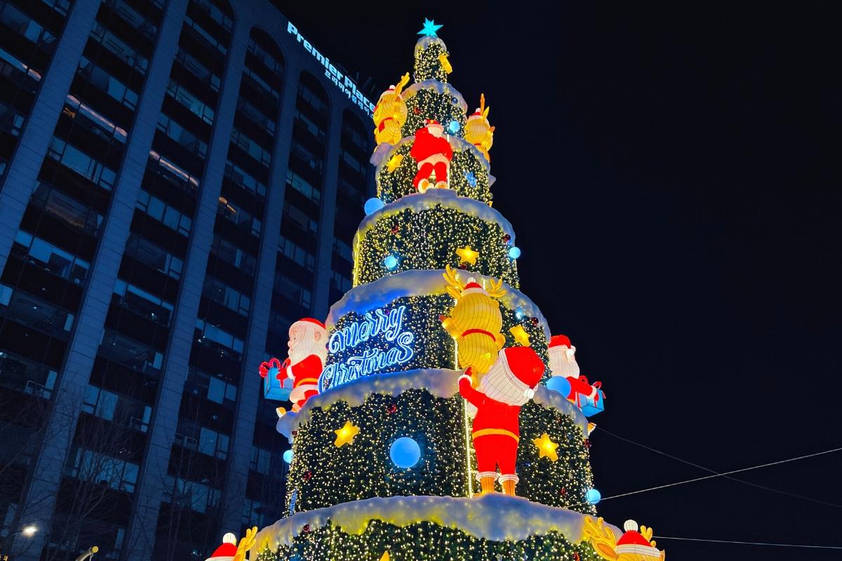 Крупный план рождественской елки с яркими огнями на фоне небоскребов