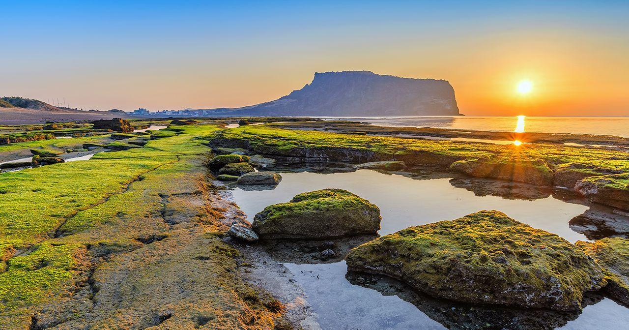 濟州島一處海岸和山嶺的清晨景色，陽光映照在海面上。