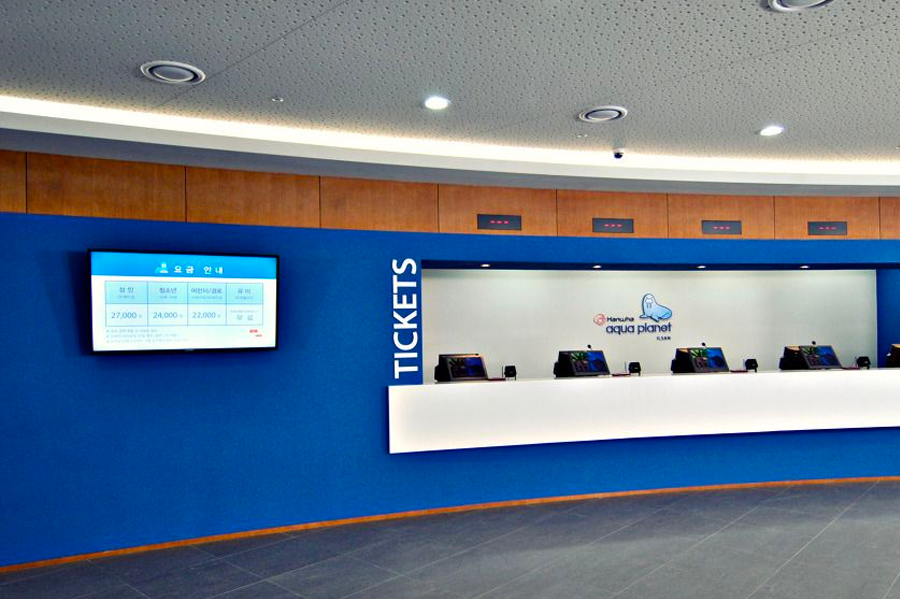 韩国海洋世界水族馆内的票务柜台，一排现代化的售票窗口和大屏幕显示票价信息，为游客提供便利的购票服务。